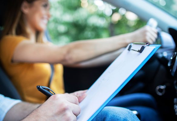 close-up-view-driving-instructor-holding-checklist-while-background-female-student-steering-driving-car